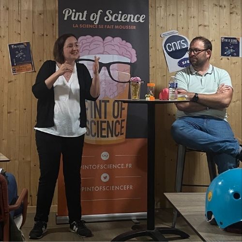 Laura André et Victorien Jeux présentent leurs travaux de recherche sans support ! Ils sont installés devant un kakémono aux couleurs du festival Pint of Science.